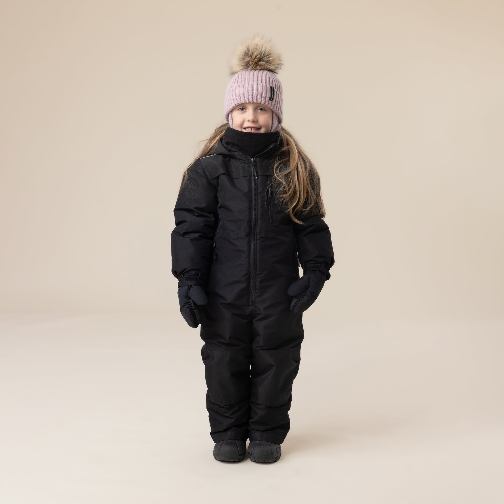 Habit de neige 1 Pièce - Peluche & Tartine (Copie) noir pour enfant, vue de face, porté par une fillette avec bonnet rose à pompon, gants noirs.