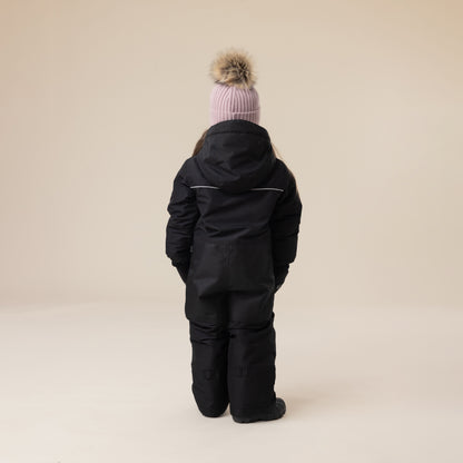 Habit de neige 1 Pièce - Peluche & Tartine (Copie) noir, combinaison une pièce pour enfant, vue de dos avec capuche, coton ou textile épais, enfant portant un bonnet rose à pompon.