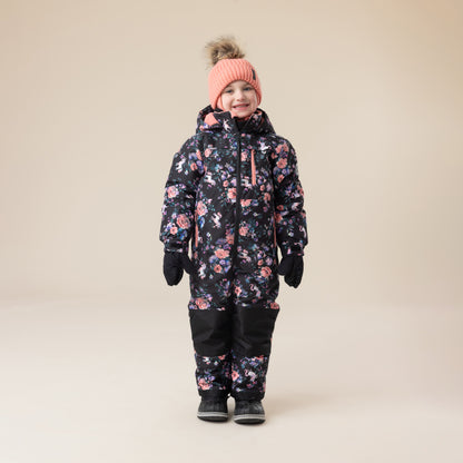 Habit de neige 1 Pièce - Peluche & Tartine, combinaison noire à motifs floraux roses et mauves, pour enfant, vue de face portée par un garçon avec bonnet rose et moufles noires.
