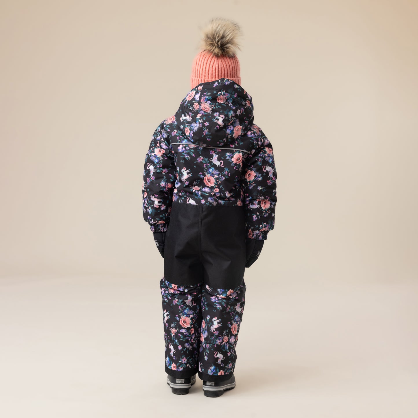 Habit de neige 1 Pièce - Peluche & Tartine pour enfant, combinaison noire avec imprimé floral rose et bleu, vue de dos portée avec bonnet rose à pompon.