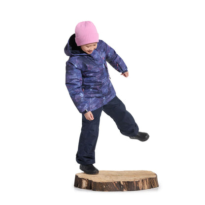 Enfant en mouvement avec bonnet rose veste violette pantalon bleu marine et bottes noires sur une souche en bois