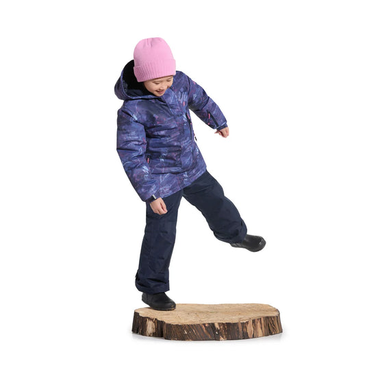 Enfant en mouvement avec bonnet rose veste violette pantalon bleu marine et bottes noires sur une souche en bois