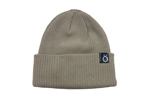Tuque d'hiver - Snö en maille beige avec revers côtelé et petit écusson noir sur le côté, vue de face.