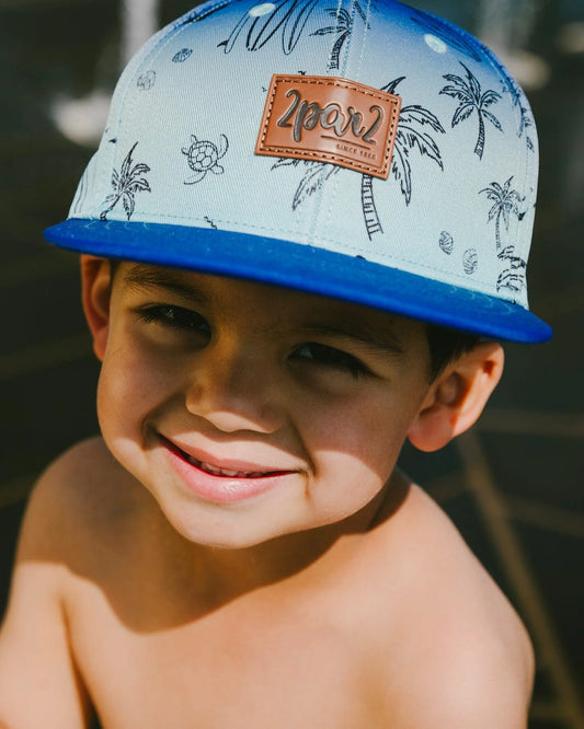 Casquette - Deux Par Deux bleu clair à imprimé plage noir et visière bleue, portée par garçon vue de face en extérieur