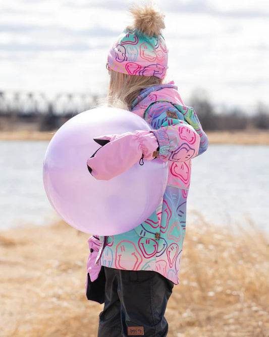 Tuque Mi-Saison - Deux Par Deux multicolore avec pompon beige amovible, polyester et élasthanne, portée par enfant de dos près d’un lac.