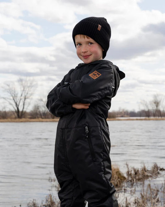 Tuque Mi-Saison - Deux Par Deux noire en tricot côtelé, enfant garçon, portée de face en extérieur près de l'eau.
