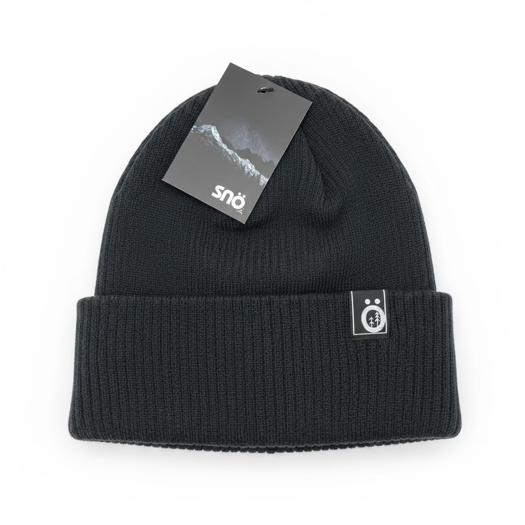 Tuque d'hiver - Snö en tricot noir avec revers épais et étiquette logo blanche, vue de dessus sur surface en bois.