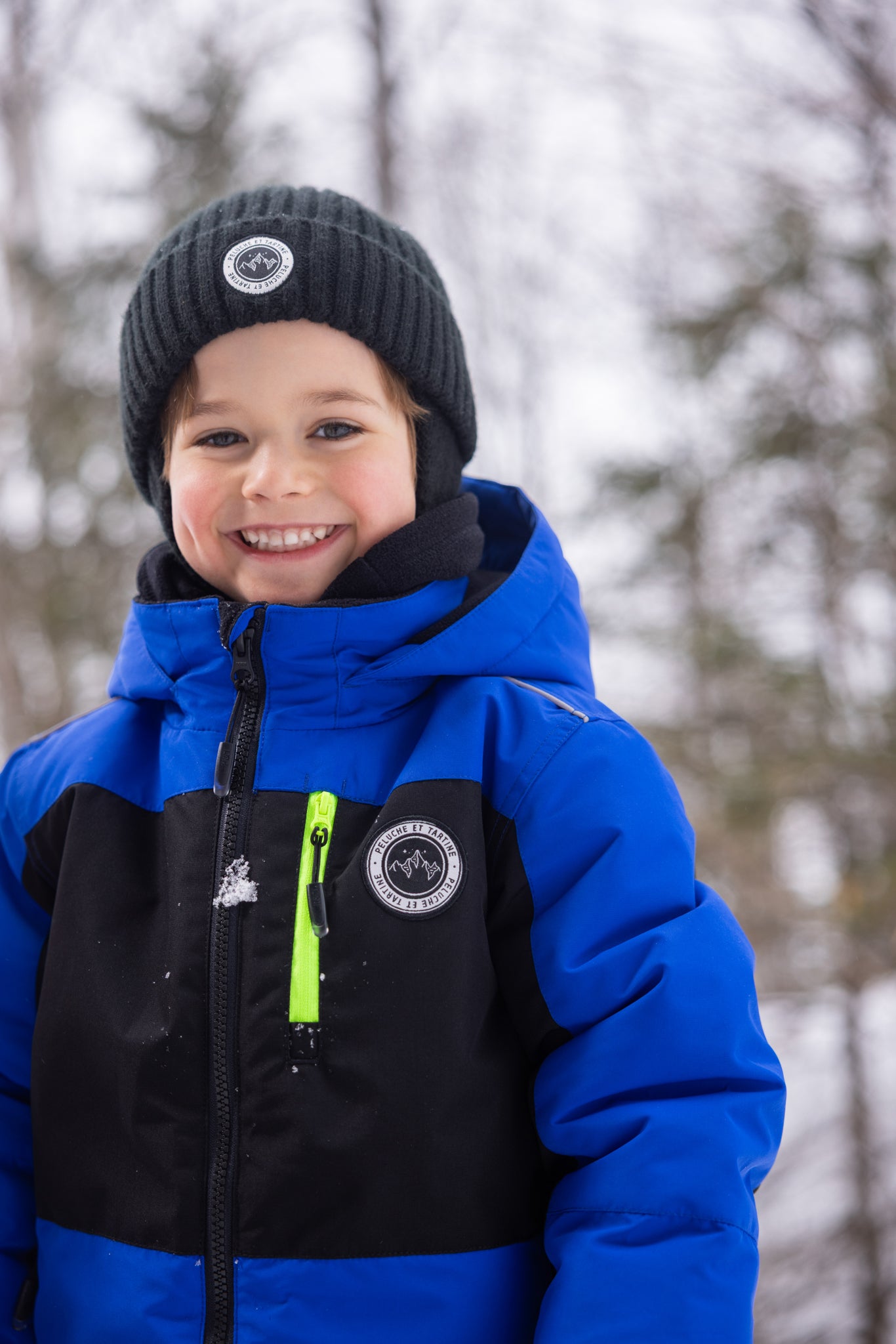 Habit de neige - Peluche & Tartine bleu et noir avec détails jaunes, veste chaude pour enfant, vue de face portée, bonnet noir en laine.