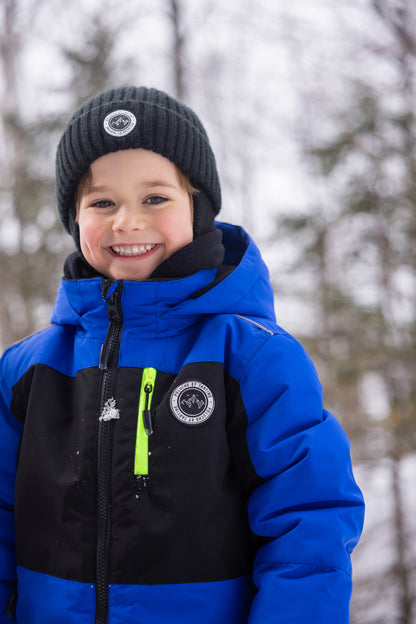 Habit de neige - Peluche & Tartine bleu et noir avec détails jaunes, veste chaude pour enfant, vue de face portée, bonnet noir en laine.