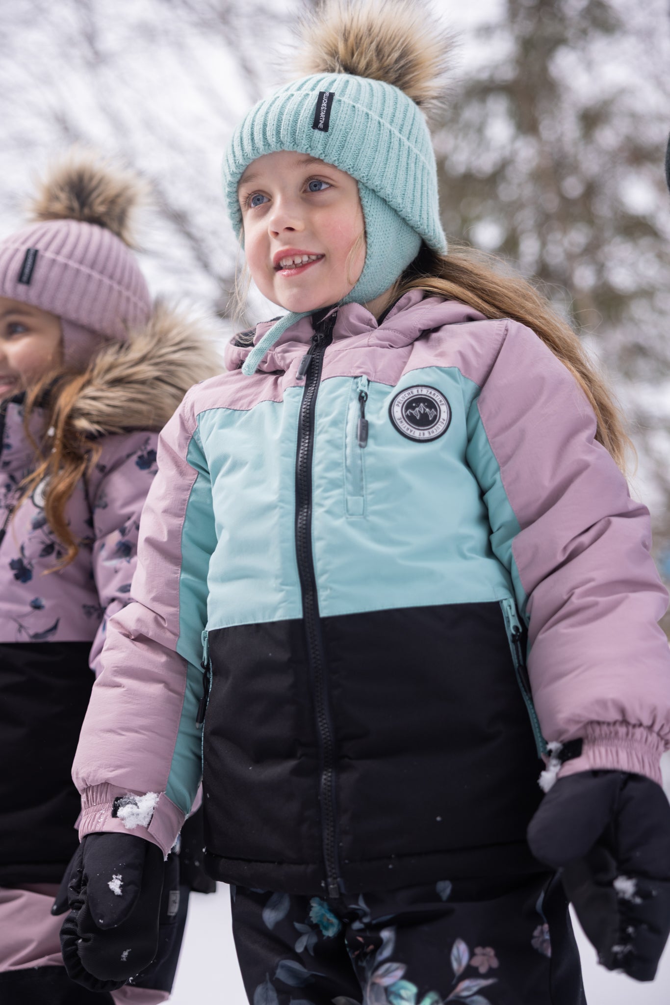Habit de neige - Peluche & Tartine, veste d’hiver tricolore rose pâle, bleu clair et noir en matériau isolant, pour enfant fille, vue de face portée en extérieur neigeux.