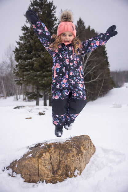 Habit de neige 1 Pièce - Peluche & Tartine à motifs floraux roses et violets sur fond noir, porté par une enfant avec bonnet rose, vue de face en extérieur neigeux.