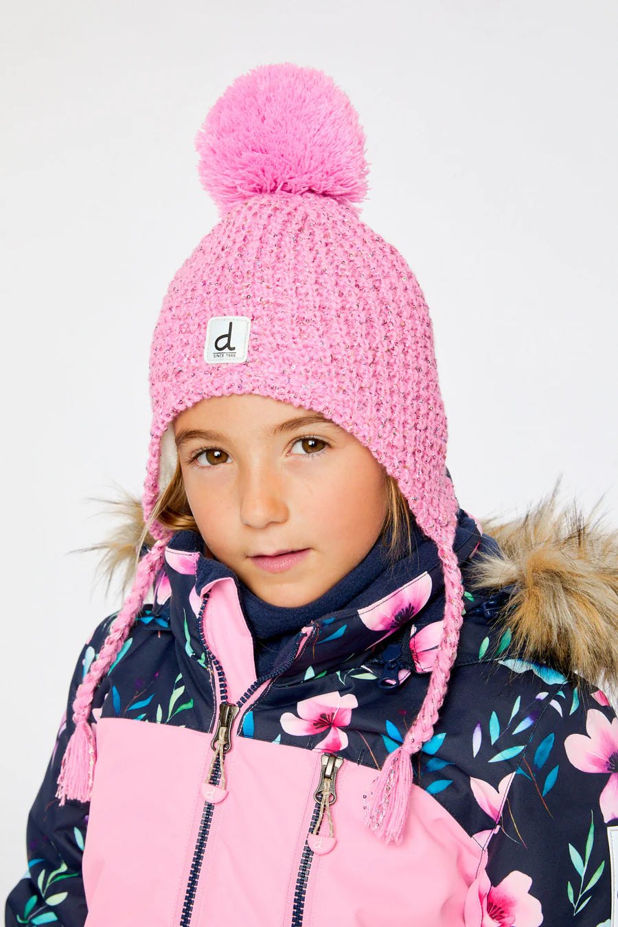 Fille portant une tuque d'hiver - Deux Par Deux rose tricotée avec pompon et tresses, manteau à capuche fourrée à motifs floraux, vue de face.