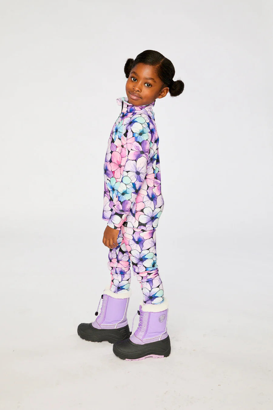 Sous-vêtements thermiques - Deux Par Deux avec motifs floraux violets, roses et bleus, pour enfant, porté de profil, en tissu chaud, avec bottes violettes.