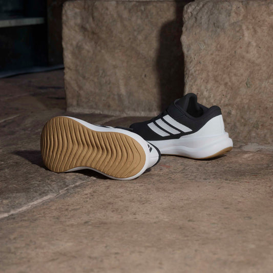 Paire de baskets de sport noires et blanches posées au sol avec semelle extérieure beige visible et vue latérale