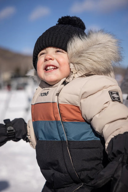 Tuque d'hiver - Nanö noire en tricot avec pompon, portée par un enfant, vue de face dans un paysage enneigé