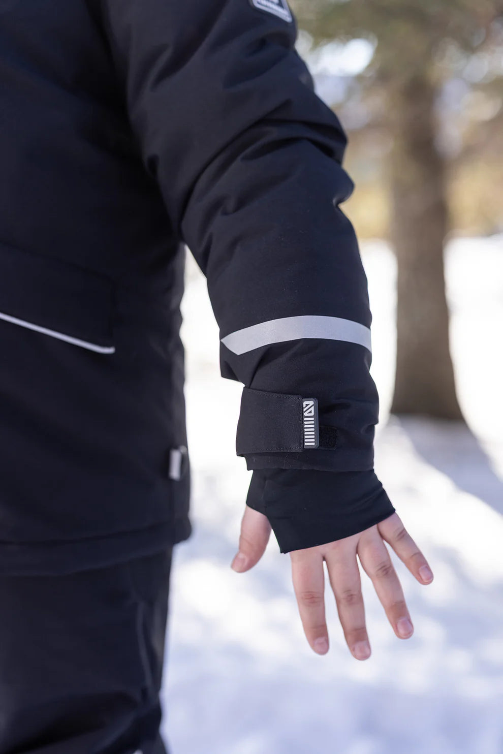 Détail de la manche noire avec bande réfléchissante et bouton-pression du Manteau d'hiver Maxifit - Nanö, porté par un enfant, vue de côté.