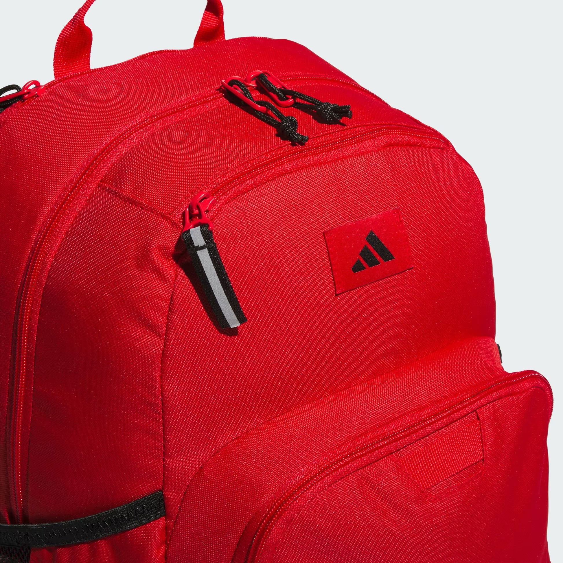 Sac à dos - Adidas rouge en tissu synthétique avec zips noirs, vue en détail du compartiment avant et du logo, style sportif unisexe.