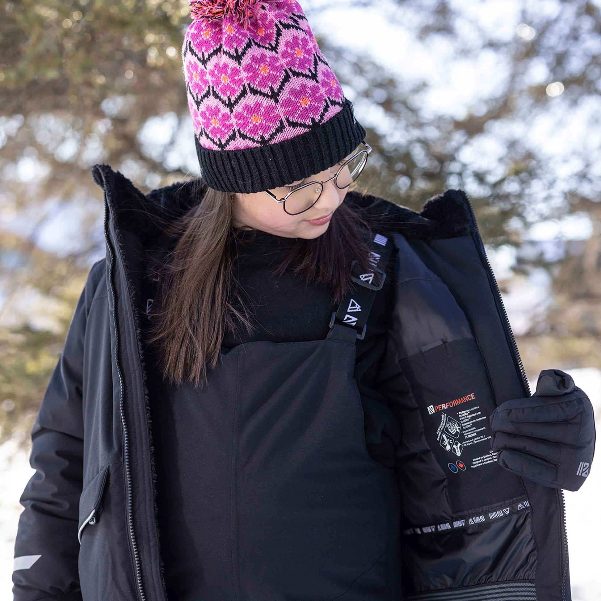 Salopette de neige Maxifit - Nanö noire en tissu imperméable, portée par une enfant, détail intérieur de la veste noire ouverte, bonnet rose à motifs, vue de face.