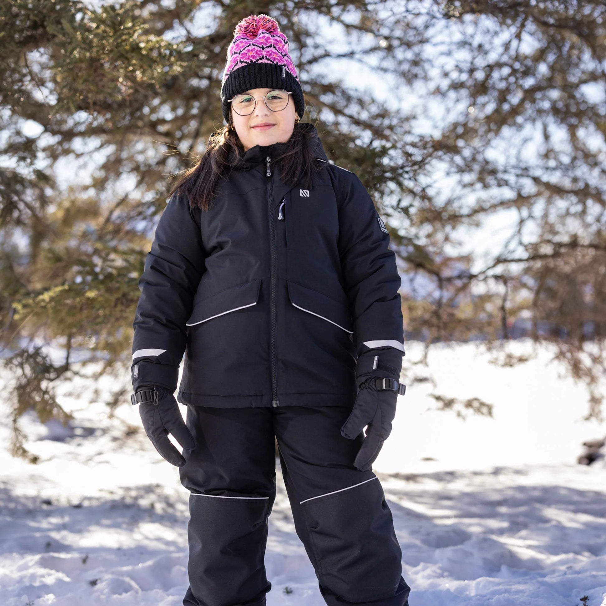 Manteau d'hiver Maxifit - Nanö noir porté par une enfant, style confortable et isolant, vue de face en extérieur enneigé avec bonnet rose et noir.