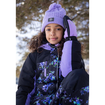 Habit de neige 1 pièce Emma - Nanö, combinaison noire et violet avec imprimé floral, portée par une enfant, vue de face en extérieur d’hiver.
