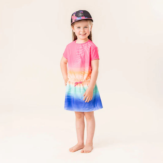Robe de plage - Nanö multicolore rose, orange, vert et bleu portée par enfant fille vue de face avec casquette noire