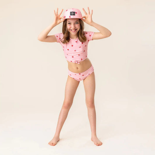 Jeune fille portant une Casquette - Nanö rose avec motif et un maillot rose à motifs, vue de face en pied.