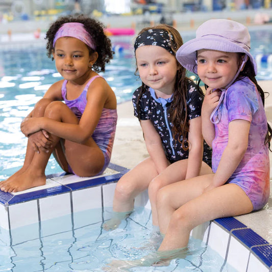 Trois filles assises au bord de la piscine, dont une portant un Chapeau U.V - Nanö violet clair, vue de profil.