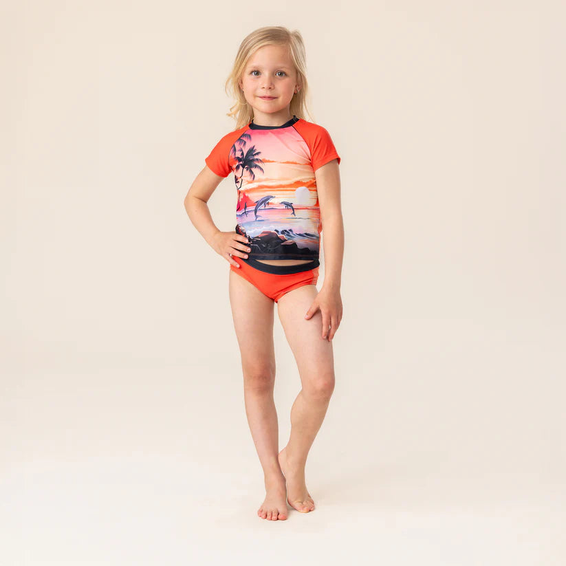 Maillot de bain - Nanö pour enfant fille, deux pièces orange avec motif coucher de soleil et palmier, vue de face porté.