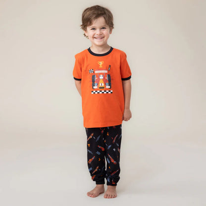 Enfant souriant portant Pyjama 3 mcx - Nanö, position galerie 2, t-shirt orange et pantalon noir à motifs imprimés.