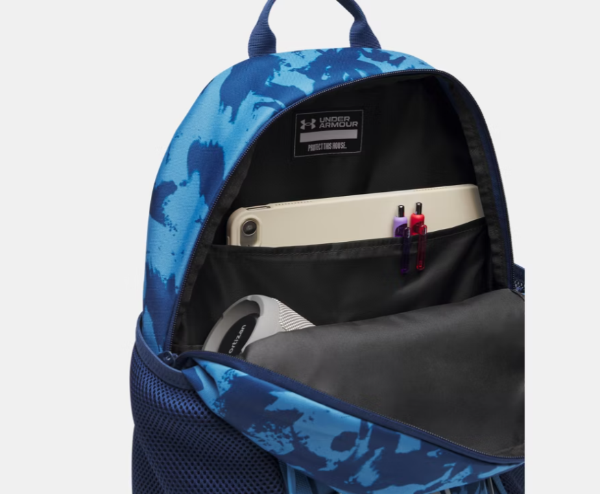 Sac à dos UA Hustle Sport 6.0 - Under Armour bleu avec motifs camouflage, compartiment intérieur ouvert montrant une tablette, des stylos et des écouteurs.
