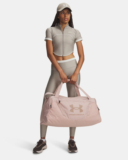 Femme tenant un Sac sport - Under Armour rose pâle, en tissu synthétique, vue de face, tenue sportive beige.