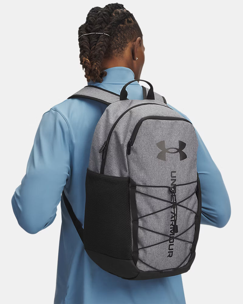 Sac à dos UA Hustle Sport 6.0 - Under Armour (Copie) gris avec noir en tissu polyester, style sportif, porté homme, vue de dos.