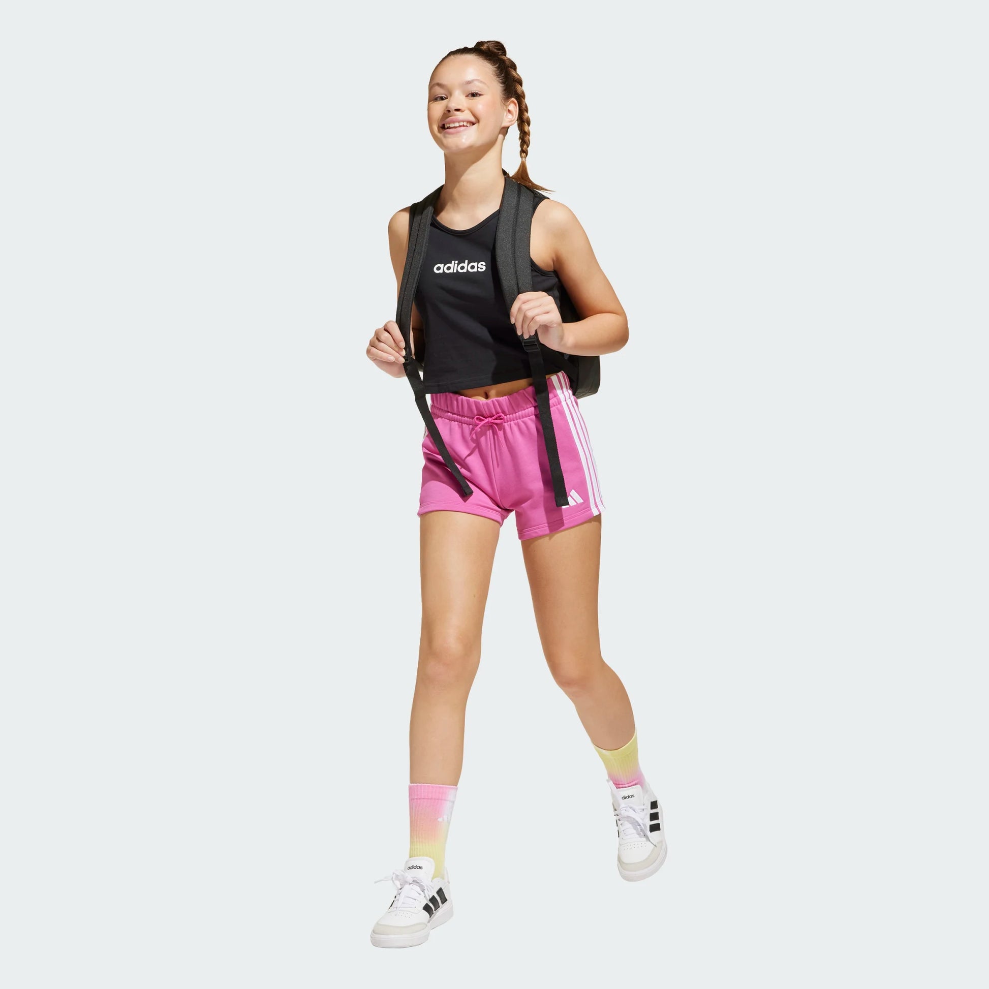 Short - Essentials Adidas rose avec bandes blanches latérales, taille élastique, pour fille, porté vue de face.