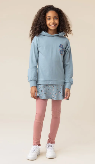 Fille portant une Tunique à capuchon - Nanö bleu clair avec motif floral sur la poitrine, manches longues, vue de face, style décontracté.