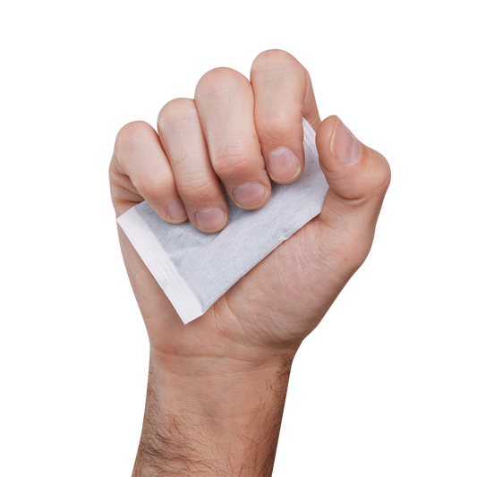 Chauffe-mains gris clair en sachet, matière textile, tenu dans une main adulte, vue rapprochée face avant