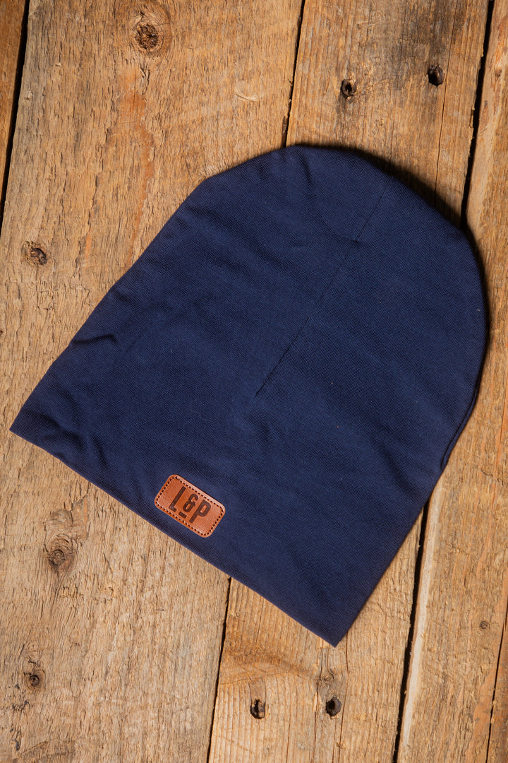 Tuque Mi-Saison - L&P bleu marine en tissu doux, extensible, logo cuir, taille enfant 2T-5T, vue de dessus sur surface boisée