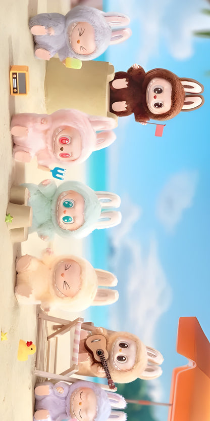 Serviette microfibre - Labubu beige posée sur sable avec jouets et peluches lapin colorés, vue de face en extérieur plage