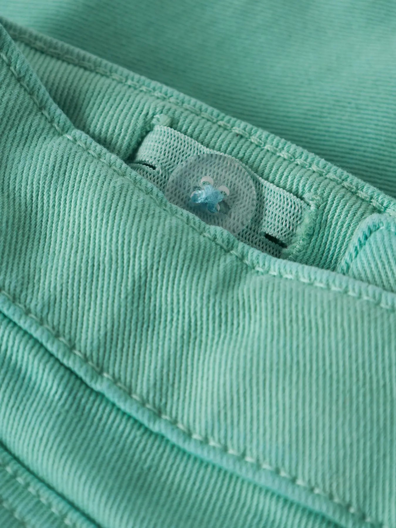 Détail bouton transparent sur tissu vert menthe en coton, Short - Name It, vue rapprochée sur couture et bouton.