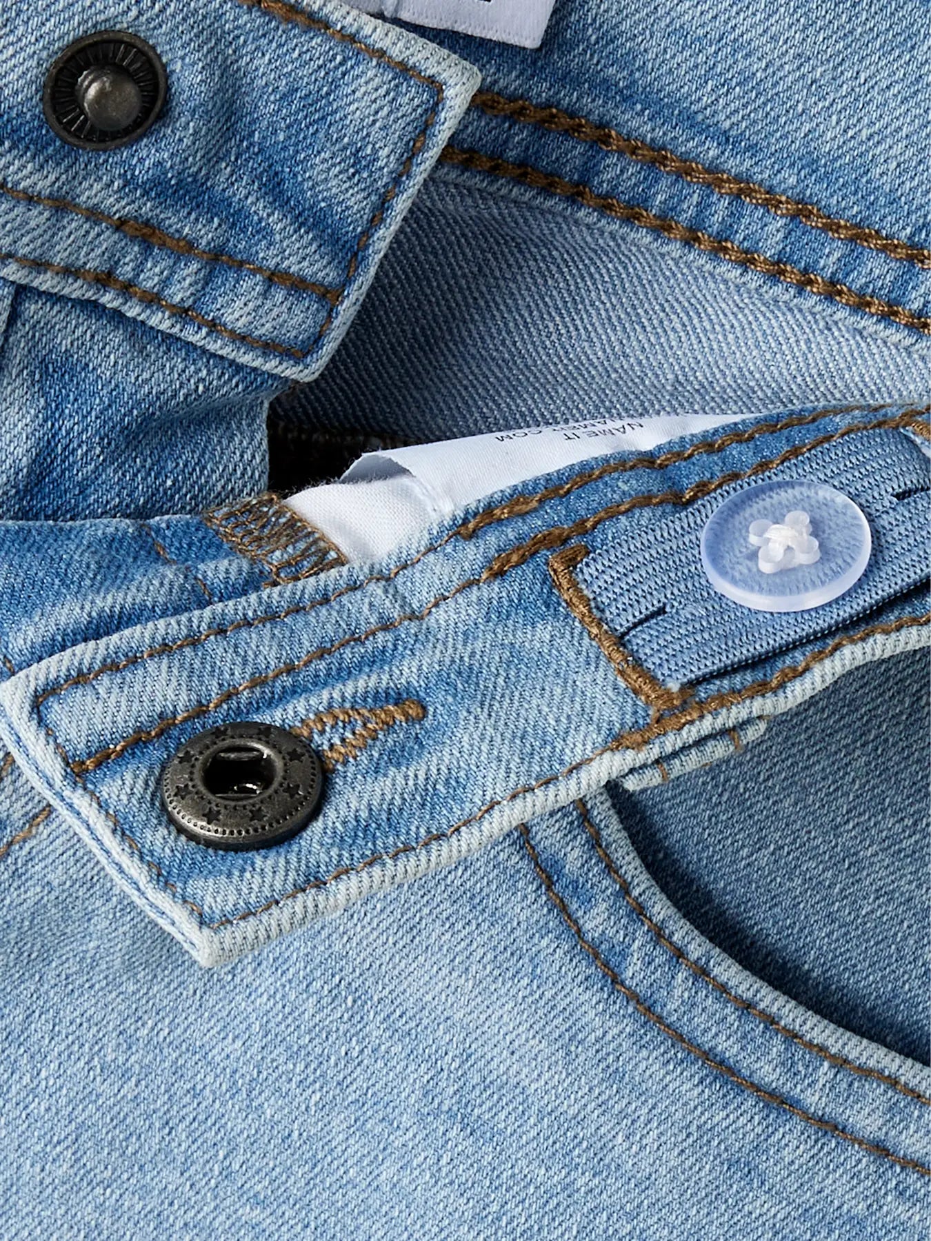 Détail du tissu en jean bleu clair avec coutures marron, boutons métalliques et plastique, Short - Name It, vue rapprochée.