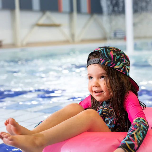 Casquette - Nanö à motif feuilles multicolores, vue portée de face sur enfant fille au bord d'une piscine.