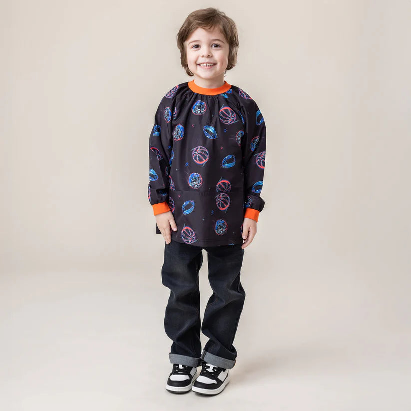 Tablier - Nanö noir à imprimés bleu et rose, col et poignets orange côtelés, pour enfant, porté de face sur mannequin garçon.