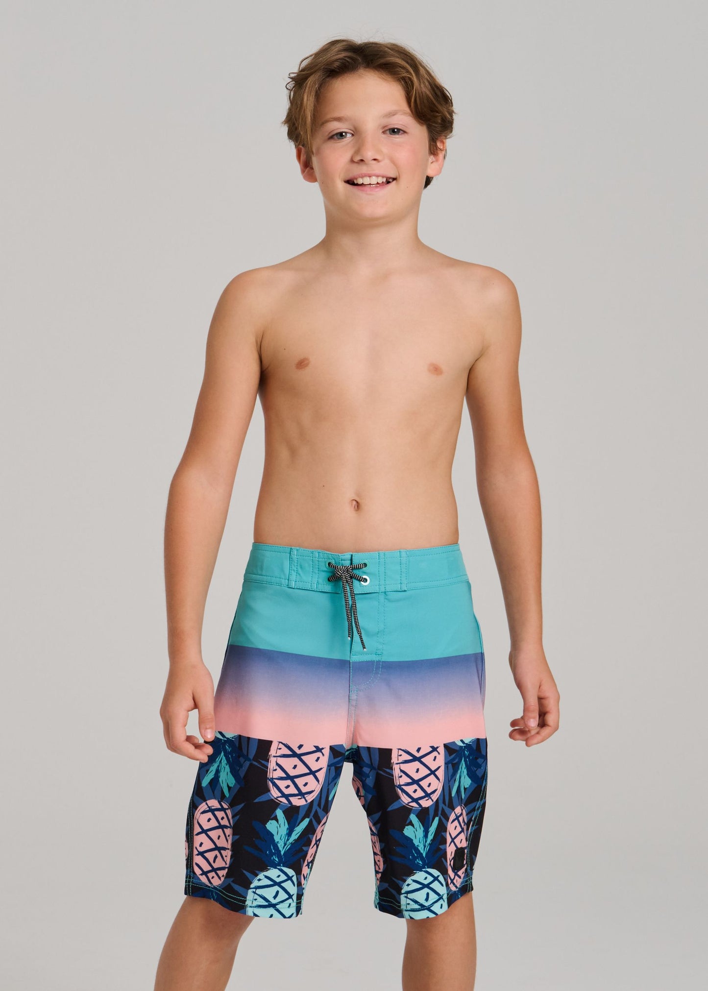 Maillot de bain - Northcoast short garçon avec motifs ananas bleu turquoise et rose, porté vue de face.