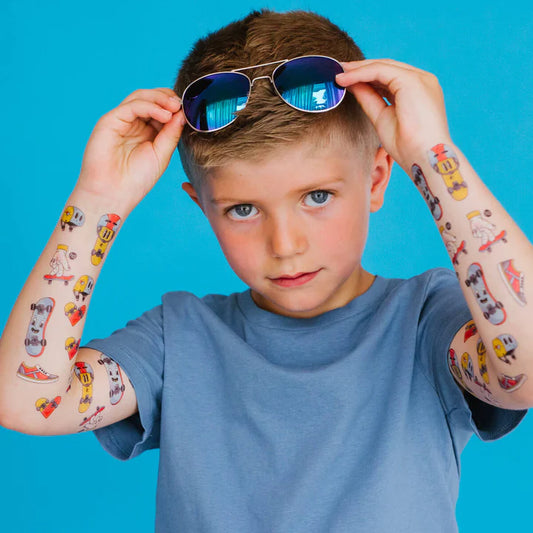 Enfant garçon portant des tatouages temporaires aux motifs colorés skate et boissons, vue de face, Pico Tatoo - Les planches en folie.