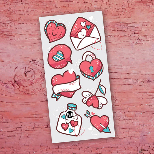 Feuille de tatouages temporaires Pico Tatoo - Saint-Valentin avec motifs rouges, blancs et bleus, vue de dessus sur fond rose.