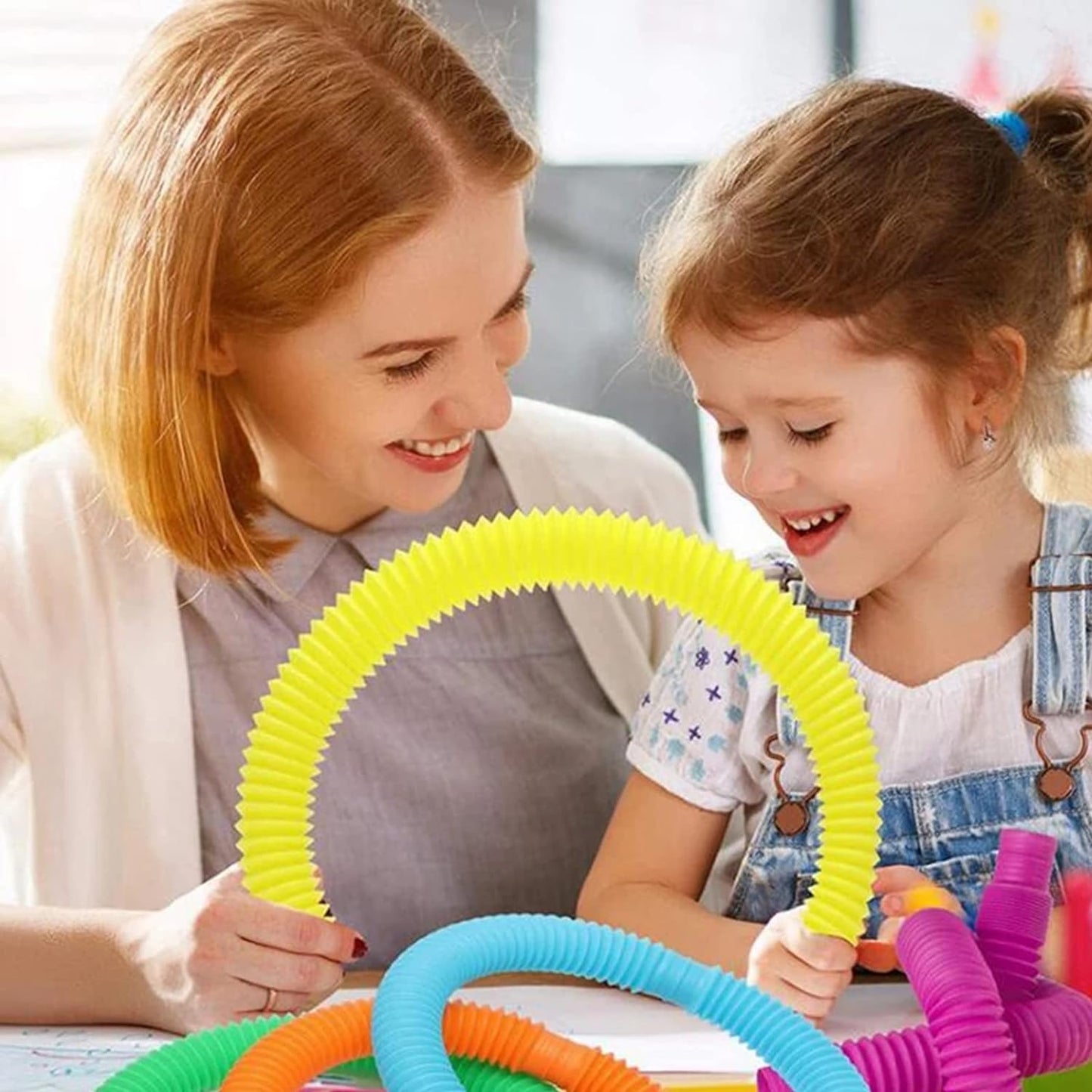 Pop Tube - Jouet sensoriel coloré en plastique souple jaune et bleu, enfant fille jouant avec adulte, vue rapprochée de face