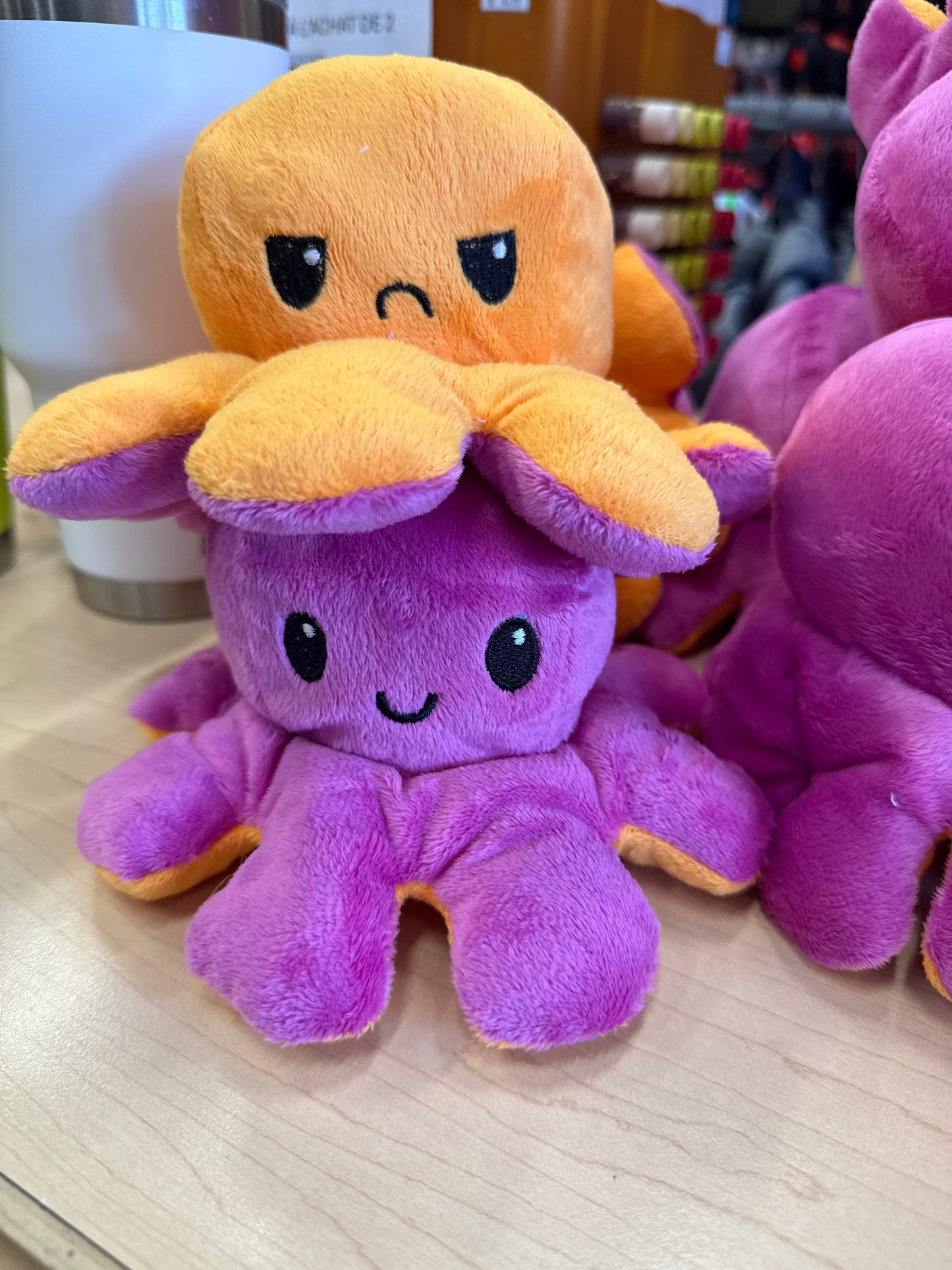 Pieuvre En Peluche Réversible violette et orange en tissu doux, style cartoon, pour enfant, vue de face sur table en bois.