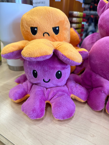 Pieuvre En Peluche Réversible violette et orange en tissu doux, style cartoon, pour enfant, vue de face sur table en bois.