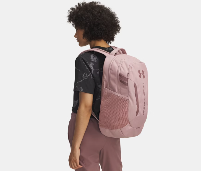 Sac à dos UA Hustle 6.0 - Under Armour rose clair avec poches latérales filet, porté dos sur jeune garçon, vue profil gauche.