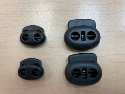 Pinces à ressorts pour lacets noires en plastique, vue de dessus, détail sur surface claire en bois.