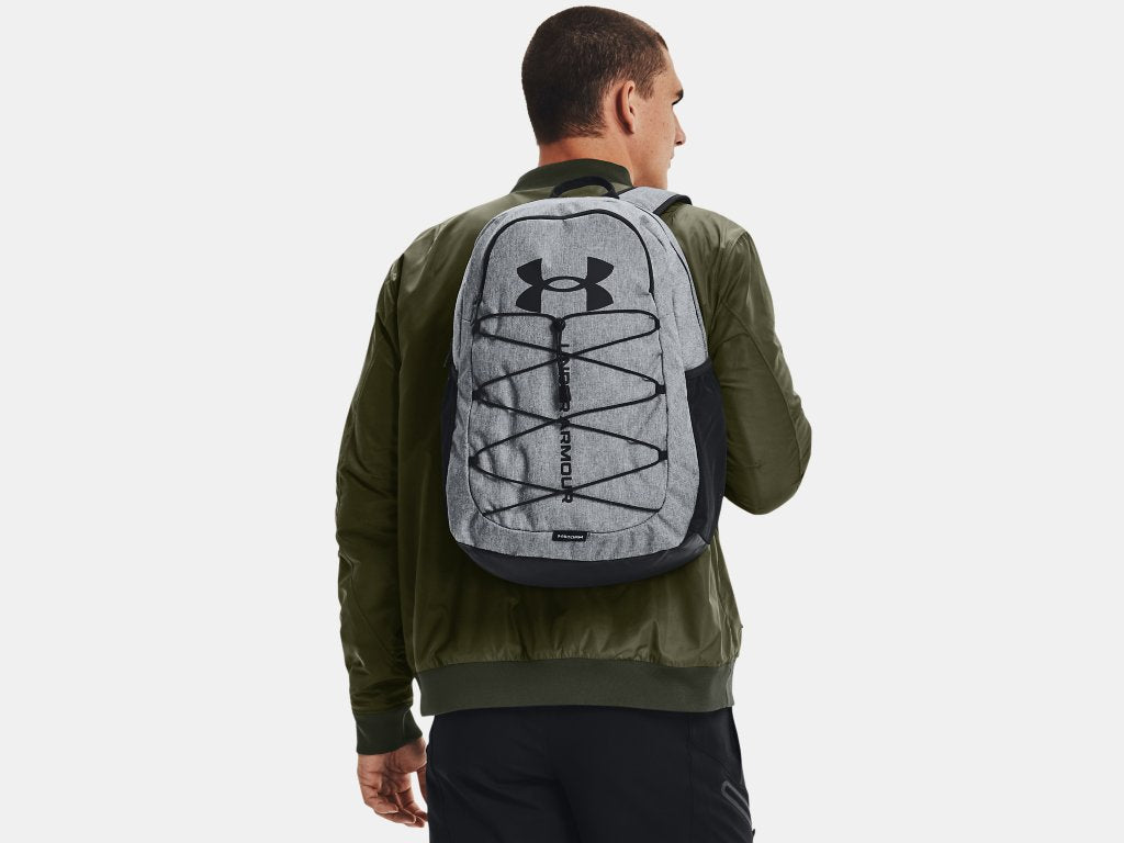 Sac à dos - Under Armour gris clair avec logo noir porté par homme de dos, style urbain, tissu imperméable visible